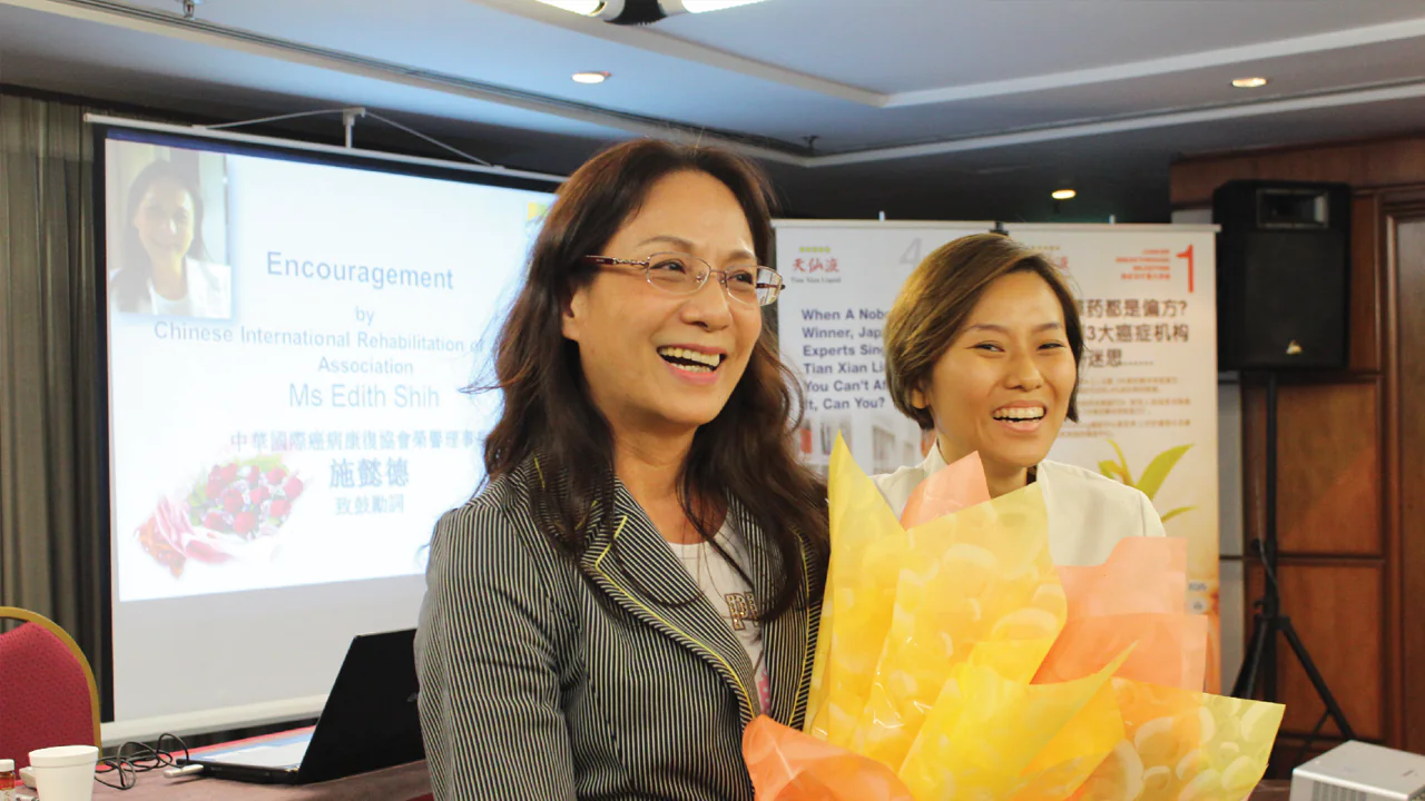 A smiling woman, Mrs. Shi from Taiwan, stands confidently outdoors, symbolizing strength and resilience as a breast and cervical cancer survivor.